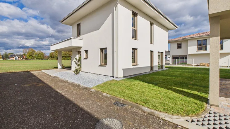Modernes Einfamilienhaus mit weißer Fassade, Carport und gepflegtem Vorgarten unter blauem Himmel.