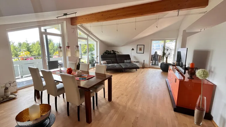 Heller Wohn- und Essbereich mit Holzbalken, Parkettboden und Zugang zum Balkon unter Dachschräge.