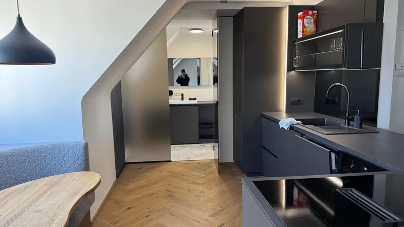 Moderne Küche mit dunklen Schränken, Induktionskochfeld und integrierter Essecke unter Dachschräge.