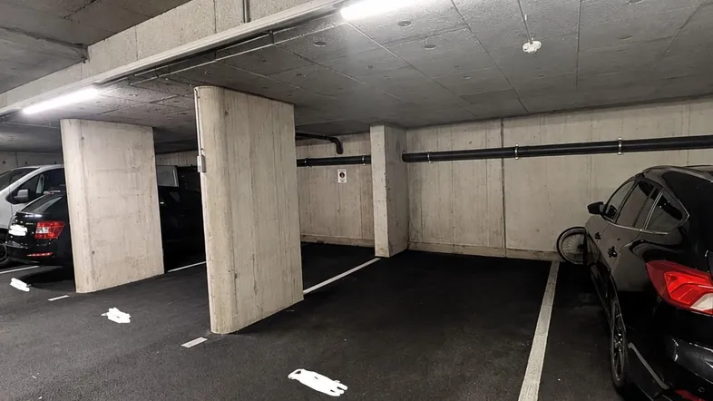 Tiefgarage mit Betonwänden und -decken, beleuchtet durch Neonröhren, bietet Stellplätze für Fahrzeuge.