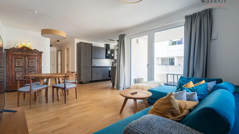 Heller offener Wohn-Essbereich mit moderner Küche, Holzboden und Zugang zum Balkon.