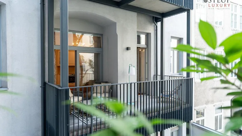 Balkon mit Metallgeländer und Blick auf den Innenhof, umgeben von grünen Pflanzen.