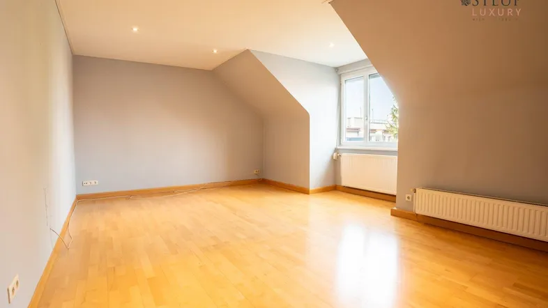 Helles Zimmer im Dachgeschoss mit Holzboden und schrägen Wänden, ideal als Wohn- oder Schlafbereich.
