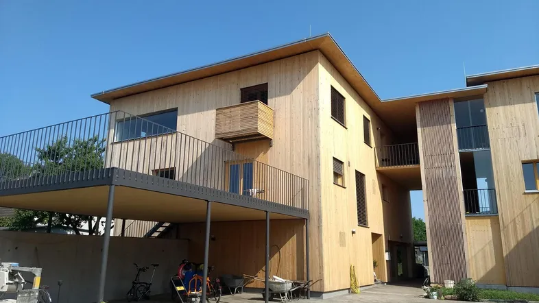 Modernes Gebäude mit Holzfassade, Balkonen und einem überdachten Carportbereich.