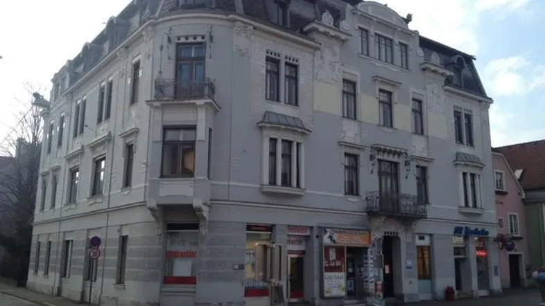 Historisches Eckgebäude mit aufwendiger Fassade, Mansarddach und kleinen Balkonen in städtischer Umgebung.