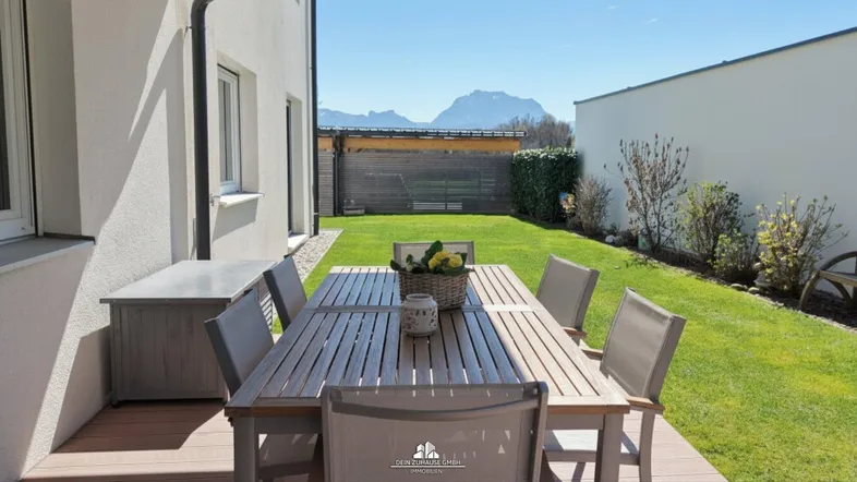 Sonniger Gartenbereich mit Holztisch und Stühlen, umgeben von Rasen und einer Hecke.