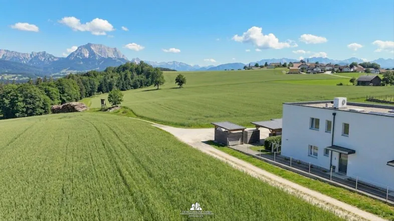 Luftaufnahme eines modernen Gebäudes umgeben von grünen Feldern mit Bergblick und Carports.