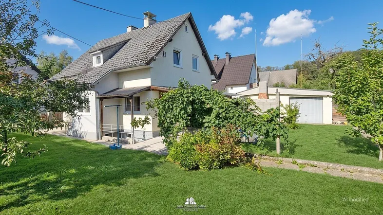Ansicht des Einfamilienhauses von der Gartenseite mit gepflegtem Rasen und Bäumen unter blauem Himmel.