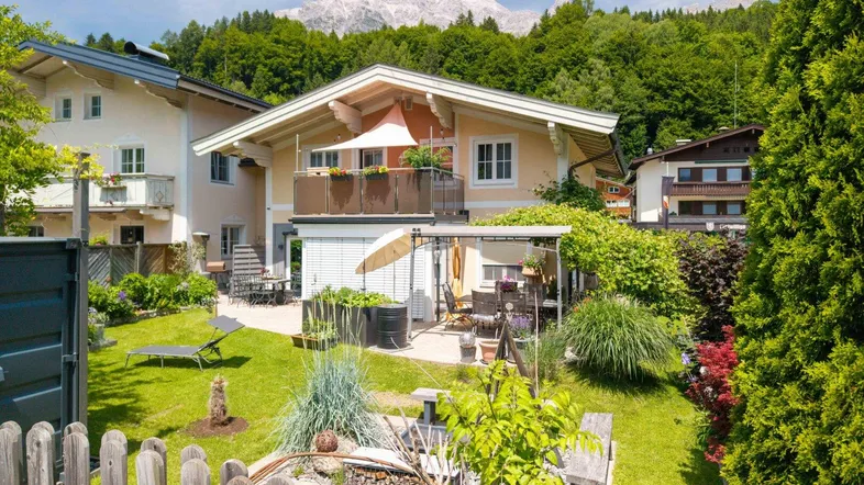 Charmantes Haus mit gepflegtem Garten, Terrasse und Balkon, umgeben von grüner Natur und Bergen.