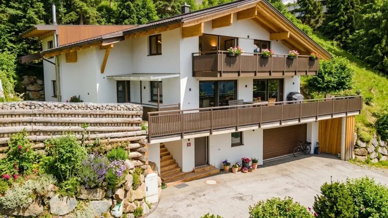 Traditionelles Alpenhaus mit Holzbalkonen und gepflegtem Garten in Hanglage.