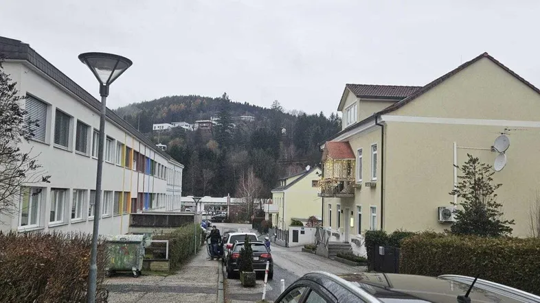 Blick auf die Straße und die umliegenden Gebäude mit bewaldetem Hügel im Hintergrund an einem bewölkten Tag.