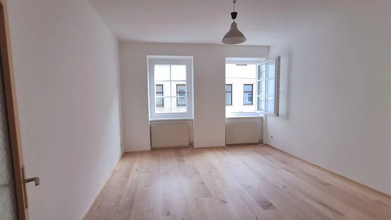 Helles Zimmer mit Holzboden und zwei Fenstern, ideal als Wohn- oder Schlafzimmer.