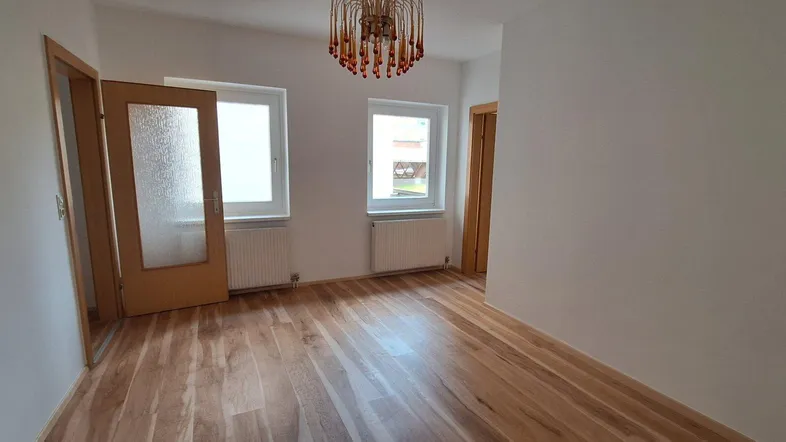 Helles Zimmer mit Holzboden und zwei Fenstern, bereit zur individuellen Gestaltung.