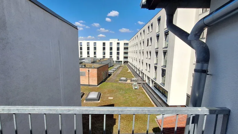 Blick von einem Balkon auf begrünte Dächer und umliegende Wohngebäude unter blauem Himmel.