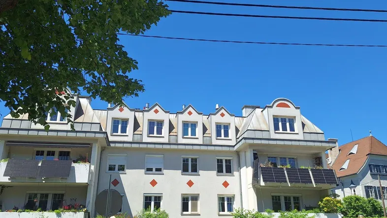 Eine moderne Wohnhausfassade mit vielen Dachgauben, Balkonen und Solarpaneelen unter blauem Himmel.