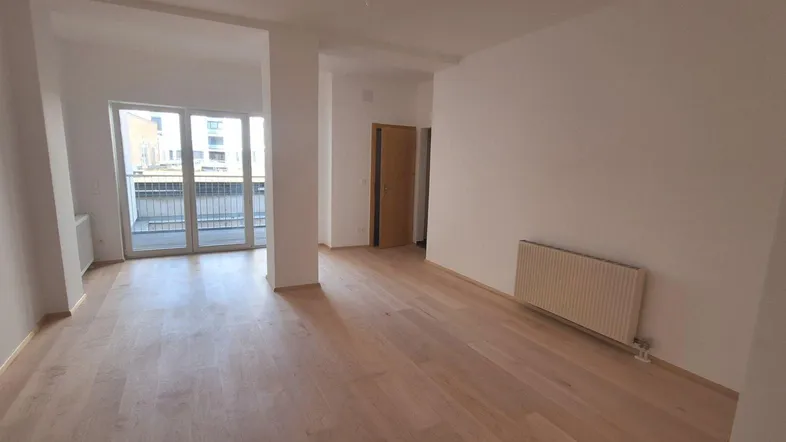 Helles, leeres Zimmer mit Holzboden und Zugang zu einem Balkon.