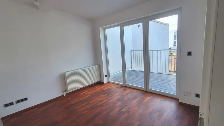 Helles Zimmer mit Holzboden und Zugang zu einem Balkon, ausgestattet mit einem Heizkörper.