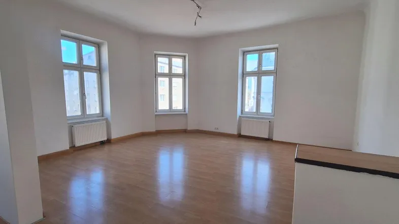 Helles Zimmer mit Holzfußboden und drei Fenstern, ideal als Wohn- oder Schlafzimmer.