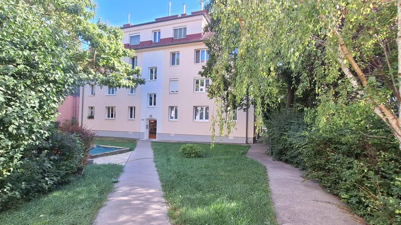 Mehrfamilienhaus mit gepflegter Fassade und grüner Umgebung, umgeben von Bäumen und Wegen.