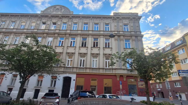 Historisches Mehrfamilienhaus mit klassischer Fassade und vielen Fenstern an einer belebten Straße.
