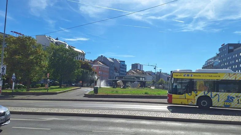 Stadtansicht mit vorbeifahrendem Bus und Gebäuden unter blauem Himmel.