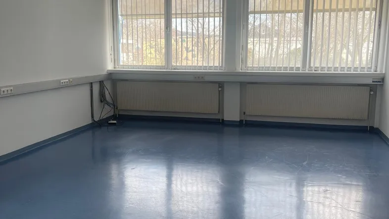 Heller, leerer Büroraum mit großen Fenstern und blauem Vinylboden, bereit zur individuellen Gestaltung.