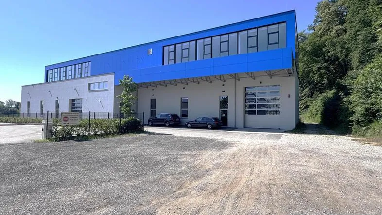 Modernes Geschäftsgebäude mit blauer Fassadenverkleidung und großem Parkplatz unter strahlend blauem Himmel.