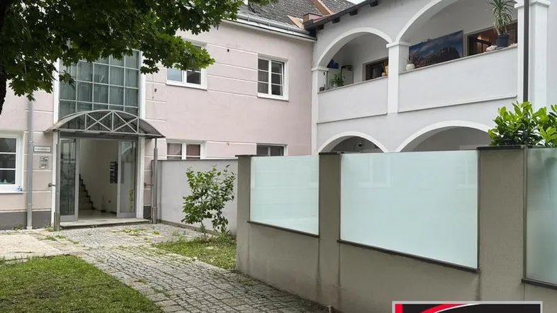 Eingangsbereich des Gebäudes mit gepflastertem Weg und begrüntem Vorgarten.
