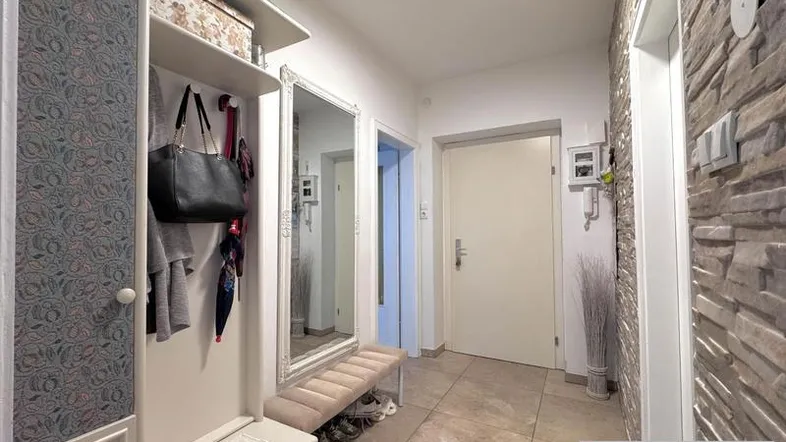 Heller Eingangsbereich mit Steinwand, Garderobe und Spiegel, der einen einladenden Empfang bietet.