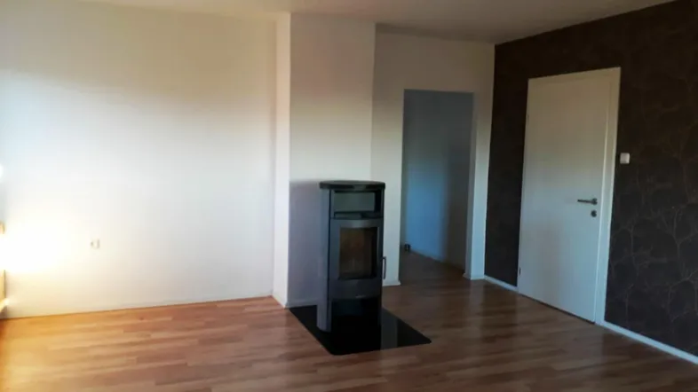 Helles Wohnzimmer mit Holzboden, modernem Kaminofen und einer dunklen Akzentwand.