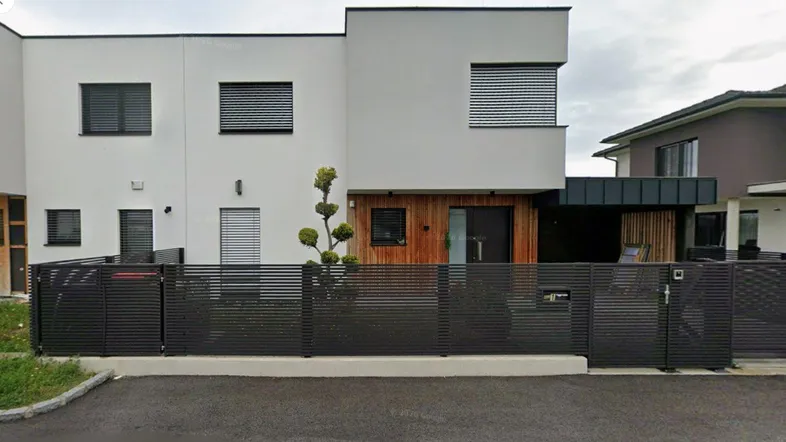 Modernes Einfamilienhaus mit weißer Fassade, Holzverkleidung und dunklem Zaun.