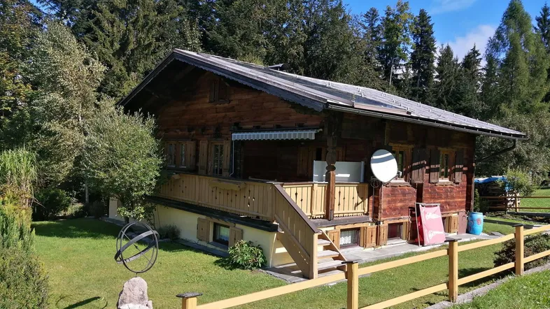 Traditionelles Holzchalet mit Satteldach, umgeben von Bäumen und einem gepflegten Gartenbereich.