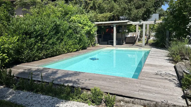 Außenbereich mit Swimmingpool und Holzdeck, umgeben von üppigem Grün und Bäumen.