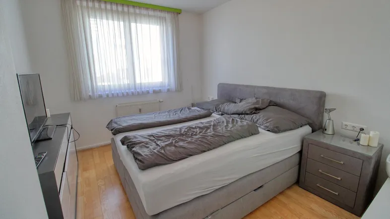 Helles Schlafzimmer mit Doppelbett, Holzfußboden und einem Fenster mit Vorhängen.