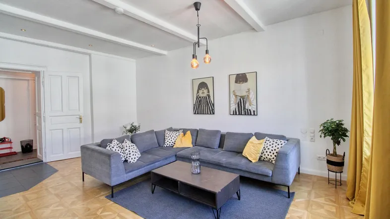 Helles Wohnzimmer mit gemütlichem Ecksofa, Parkettboden und dekorativen Deckenbalken.
