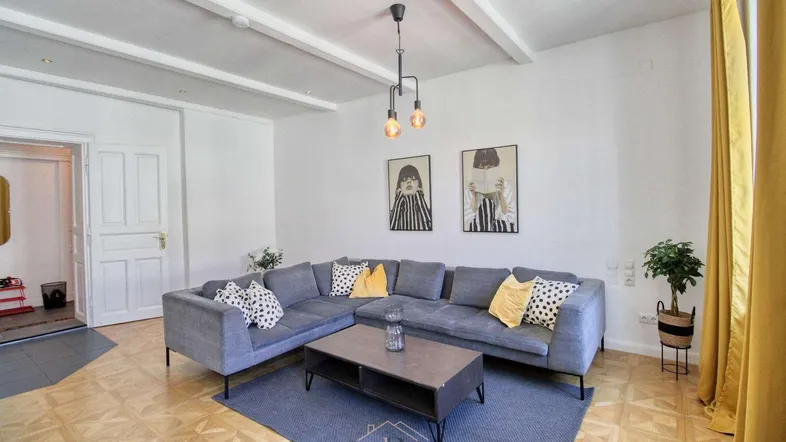 Gemütliches Wohnzimmer mit großem Ecksofa, Holzbalkendecke und hellem Parkettboden.