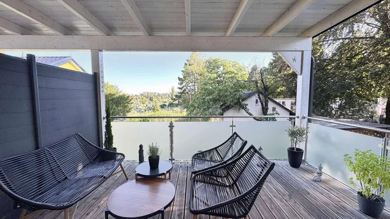 Geräumige überdachte Terrasse mit Holzdeck, bequemen Sitzgelegenheiten und weitem Blick ins Grüne.
