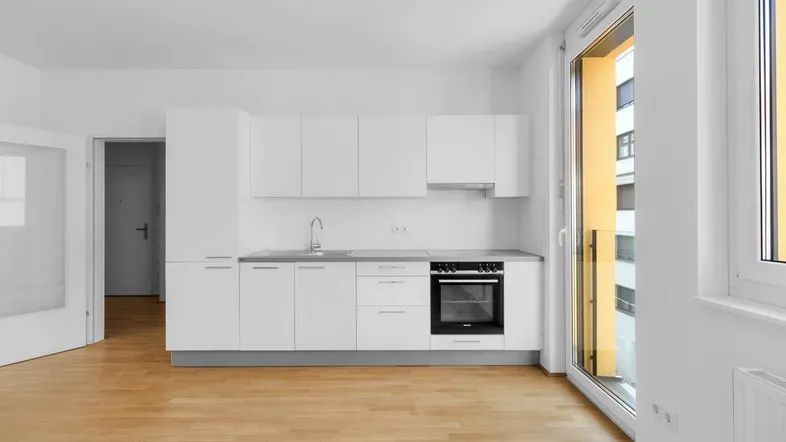 Moderne, helle Küche mit weißen Schränken, integriertem Backofen und Zugang zum Balkon.