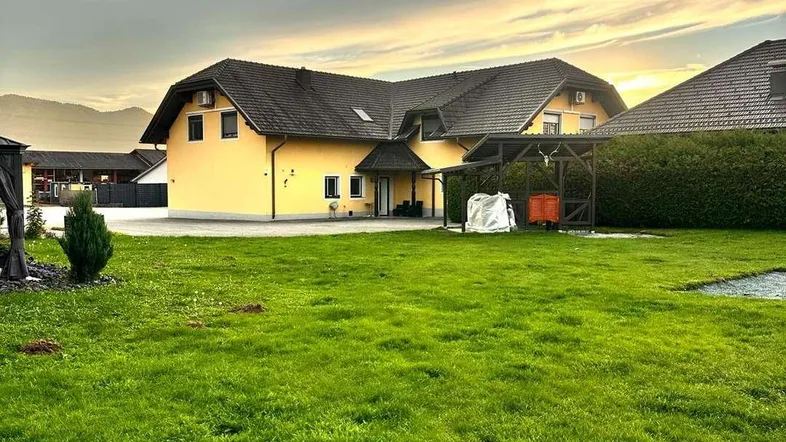 Gelbes Einfamilienhaus mit großem grünen Garten und Bergkulisse bei Sonnenuntergang.