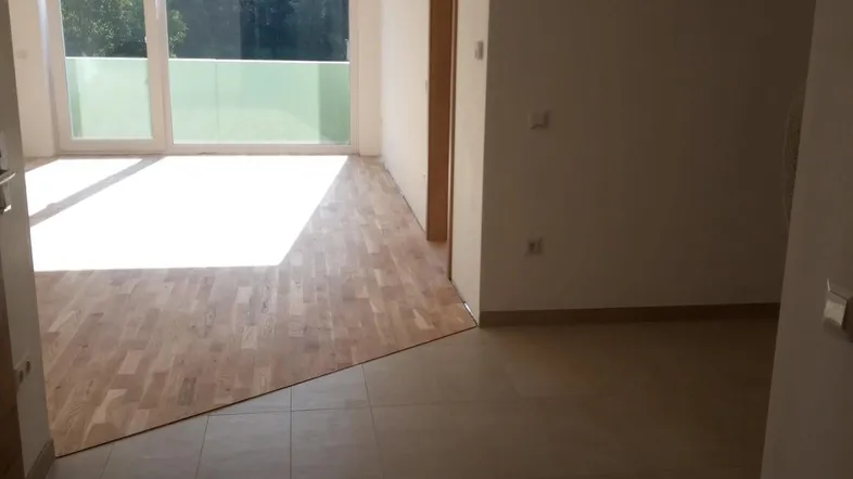 Heller Wohnbereich mit Parkettboden, Fliesen und Zugang zu einem Balkon mit viel Tageslicht.