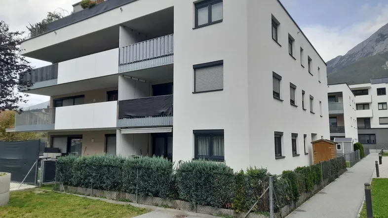 Modernes Mehrfamilienhaus mit Balkonen, Rollläden und gepflegter Hecke im Vordergrund.