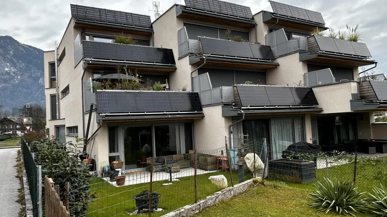 Modernes Mehrfamilienhaus mit Photovoltaikanlagen, großzügigen Balkonen und Terrassen, umgeben von Grünflächen und mit Bergblick.