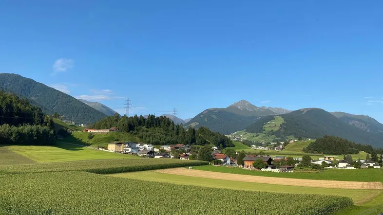 Ländliche Landschaft mit grünen Feldern, Bergen und einem kleinen Dorf unter blauem Himmel.