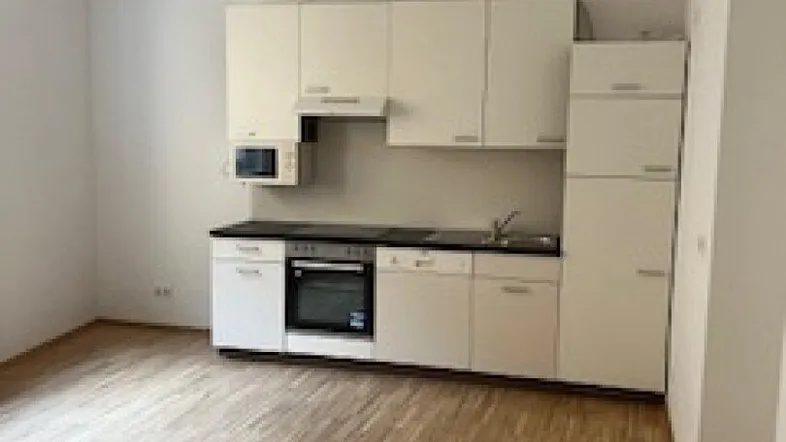 Helle Küchenzeile mit weißen Schränken, schwarzer Arbeitsplatte und Holzfußboden in einem leeren Raum.