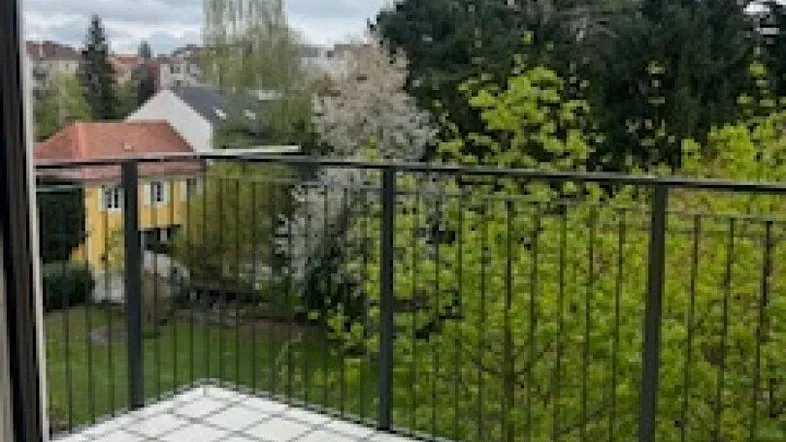 Geräumiger Balkon mit Fliesenboden und Blick ins Grüne unter bewölktem Himmel.