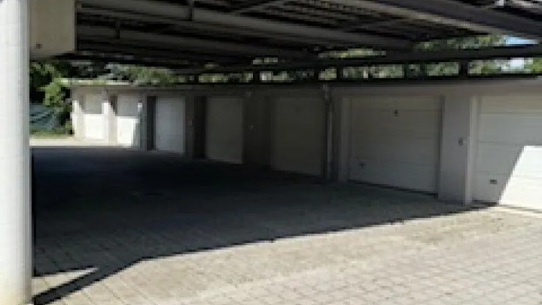 Reihe von Garagen unter einer erhöhten Struktur mit gepflastertem Vorplatz und Grünflächen.