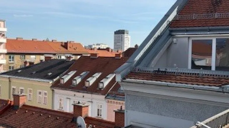 Blick über die Dächer der Stadt mit verschiedenen Gebäuden und einem hohen Gebäude in der Ferne.