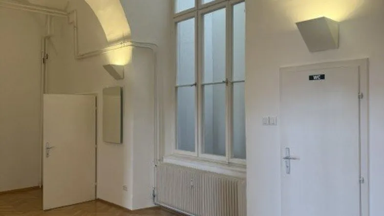 Heller Raum mit Fischgrätparkett, weiß gestrichenen Wänden und einem hohen Fenster, das viel Tageslicht hereinlässt.