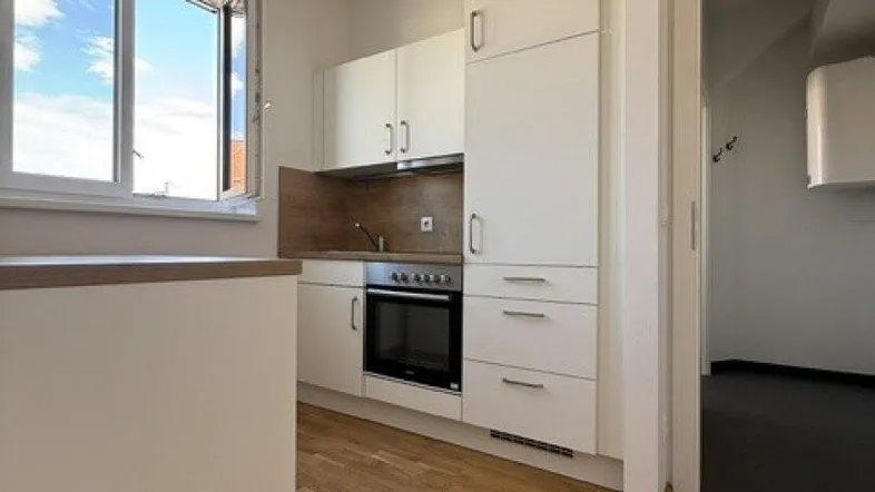 Helle Einbauküche mit weißen Schränken, Holzarbeitsplatte und Fensterblick nach draußen.