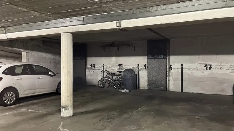 Tiefgarage mit Betonwänden, nummerierten Stellplätzen und einem geparkten Auto sowie Fahrrädern.